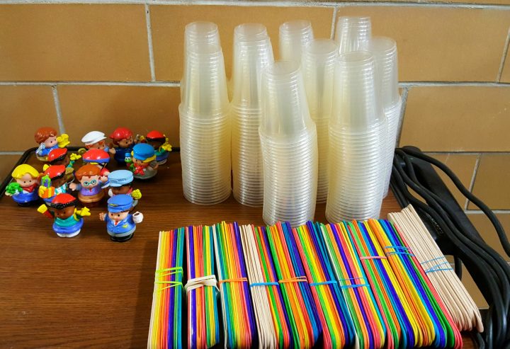 STEM challenge shows stacks of plastic cups, groups of jumbo popsicle sticks and plastic little people.