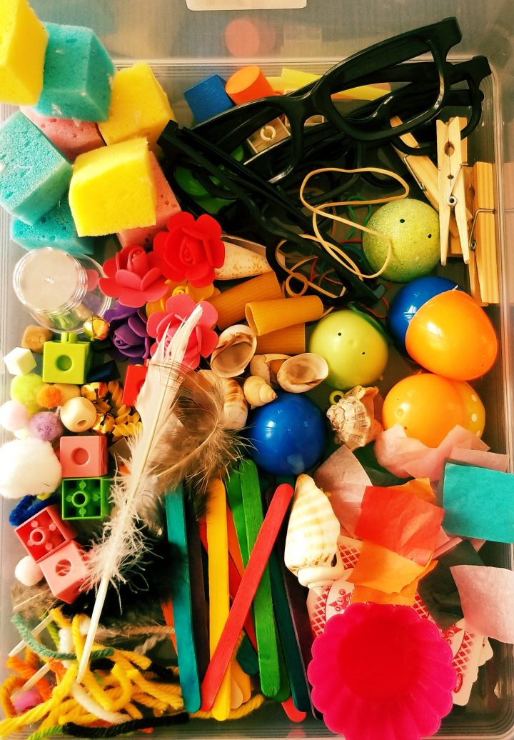 art activity for kids shows a bin with random things like clothes pin, popsicle sticks, Easter eggs, yarn and sponges.