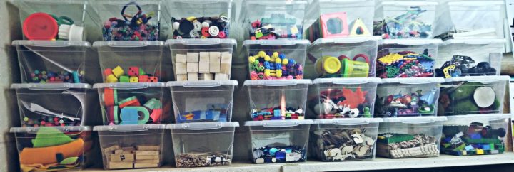 classroom shows twenty eight clear bins filled with toys and craft materials.