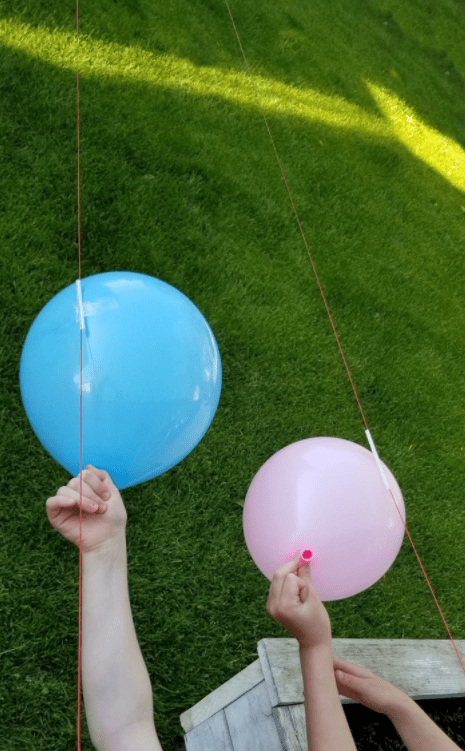 balloon rocket science experiment shows two children holding balloons attached to a string.