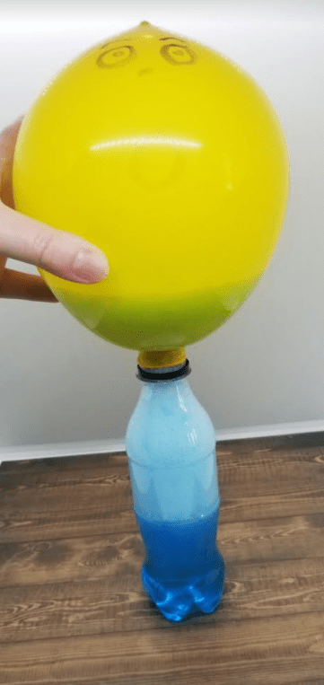 easy science experiment shows a balloon blown up on top of a plastic water bottle.
