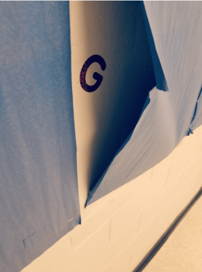letter games shows the letter G under a ripped sheet of paper on a wall.
