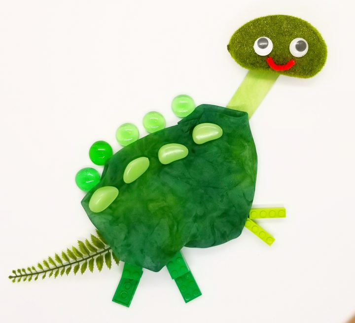 object art for kids shows a dinosaur made from fabric, beads, sticks and plants.