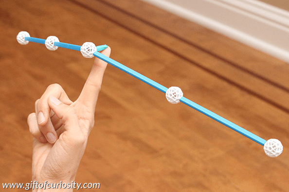 STEM challenges shows a balance beam with straws and balls balanced on a Childs finger.