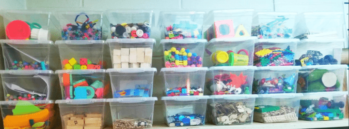 kindergarten classroom shows stacks of clear bins with crafts and little toys in each.