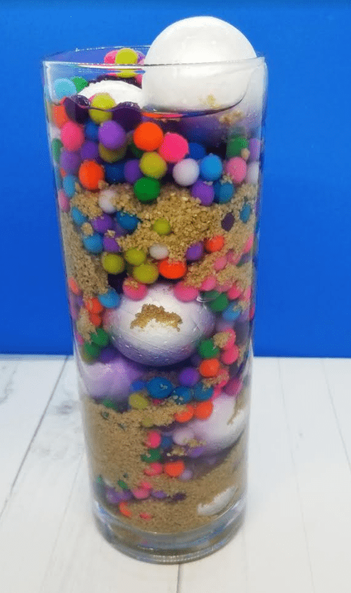 mental health lessons for kids shows a clear jar with styrofoam balls, pompoms, sand and purple liquid.