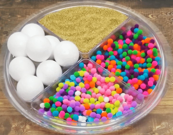 mental health lessons for kids show a container split into four with small colorful pompoms, Styrofoam balls and sand.