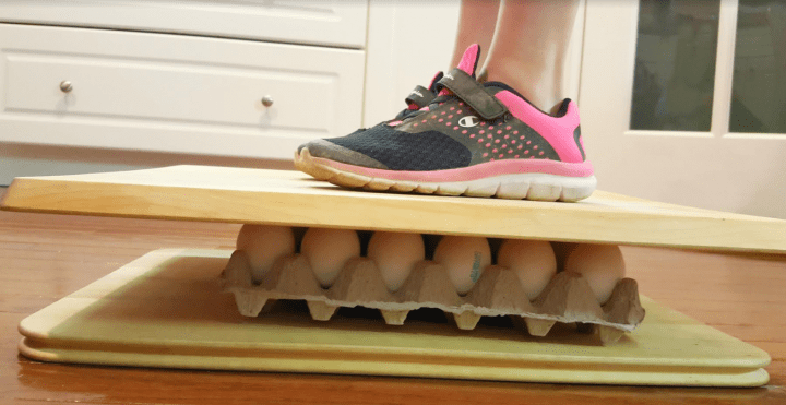 science experiments for kids shows a child standing on a tray of eggs.