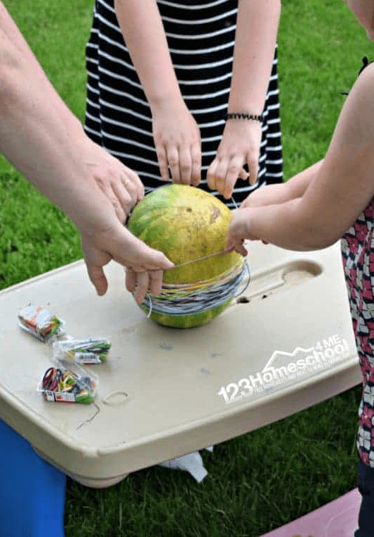 outdoor activities for kids shows children putting elastics around a watermelon.