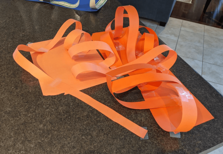 stem challenge for kids shows a roller coaster made from orange construction paper.