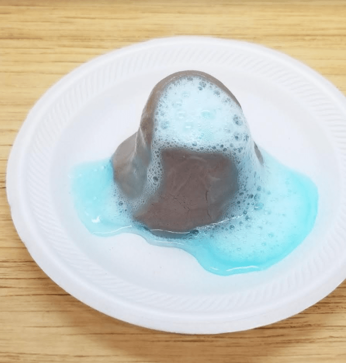 easy clay activities shows a mini clay volcano with fizzing liquid coming out.