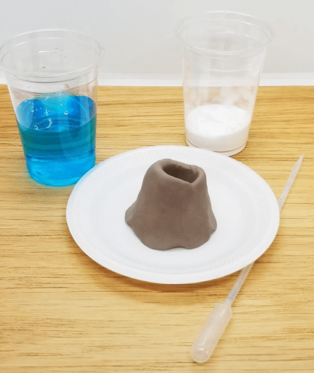 volcano experiment for kids shows a clay volcano and a liquid and powder.