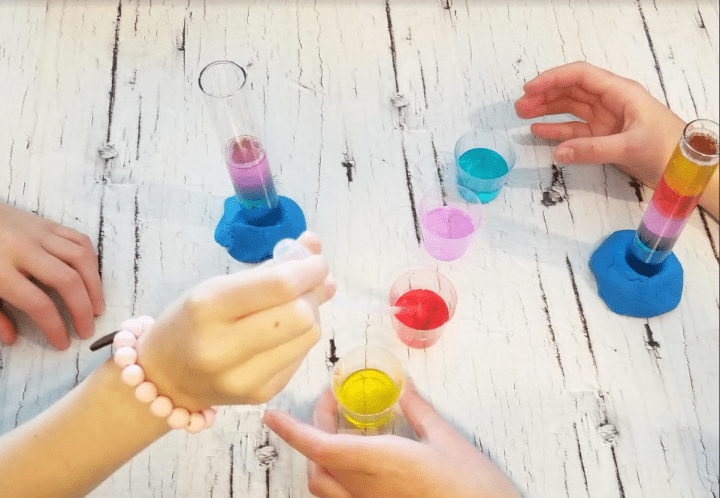 science experiments for kids shows children pouring layers of water and other colored liquids into a test tube.