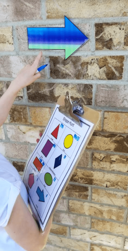shape hunt activity shows a child pointing to an arrow on a wall while holding a shape hunt sheet.