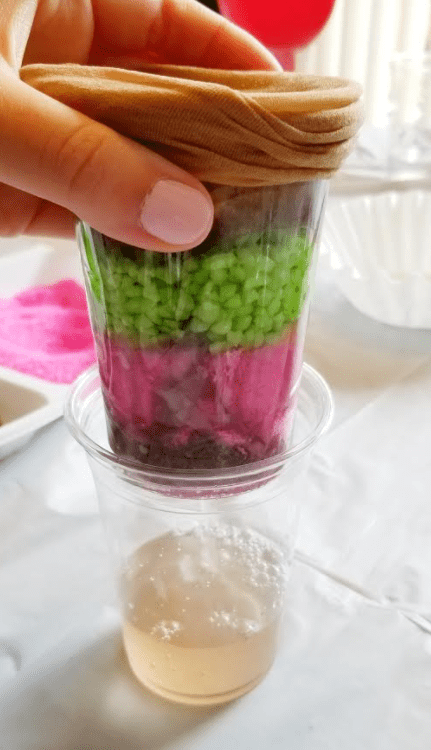 clean water experiment shows a cup with layers and slightly dirty water dripping out the bottom.