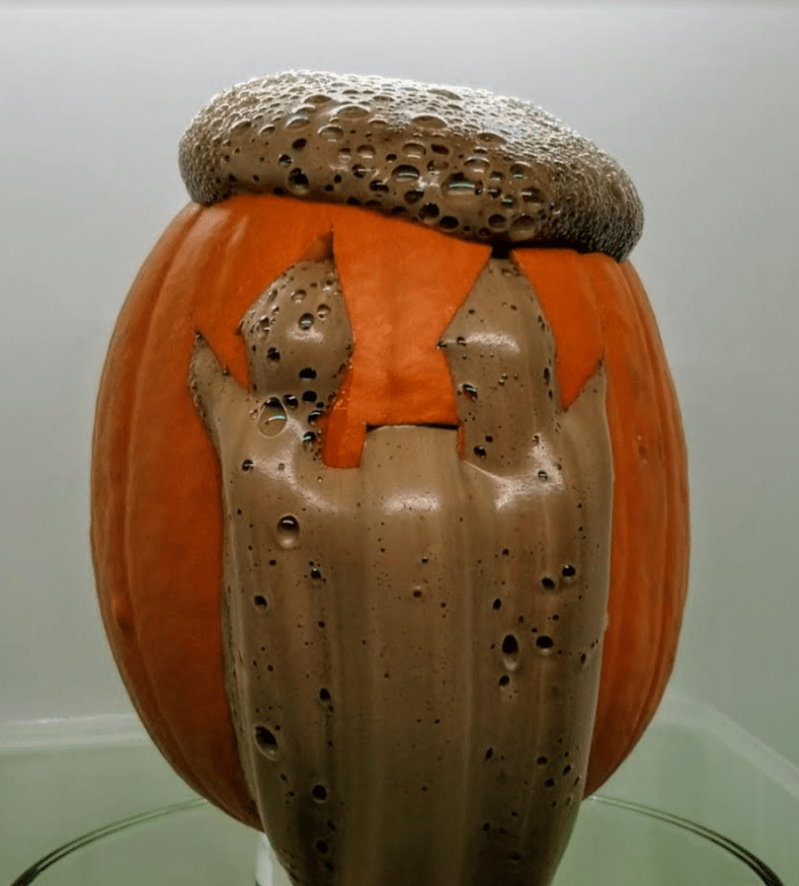 science experiment for kids shows a jack o lantern with brown foam coming out of it.