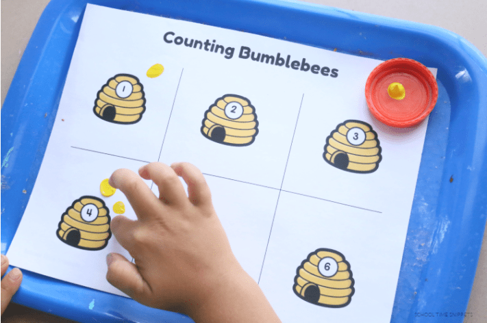 math shows a child pointing at a bee hive and putting four finger dots on it to match the number on it.