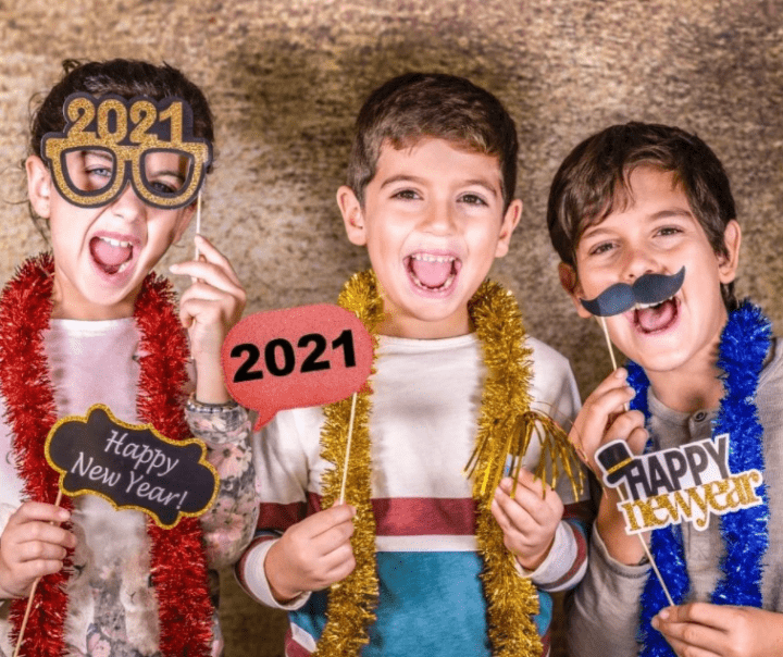 new years eve ideas for families and three boys smiling and holding photo props such as a moustache, 2021 and glasses.