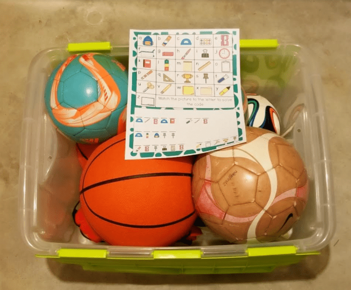 A bin of soccer, basketball and other sporting equipment with a printed escape room puzzle.