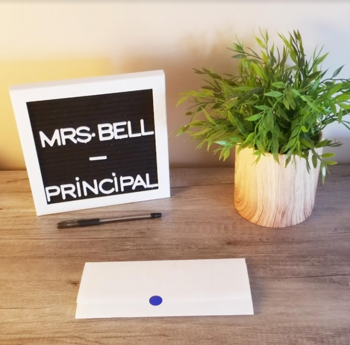 escape room for kids shows a plant and principal name tag and escape room clue on a desk.