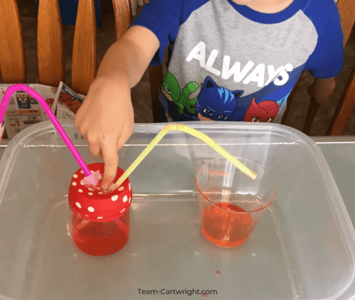 Valentines day stem activities image show a child touching a stretched balloon over a jar with straws in it.