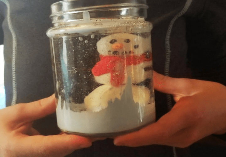 A child holding a snow globe they created with a snowman and blue paint inside for a stem science experiment