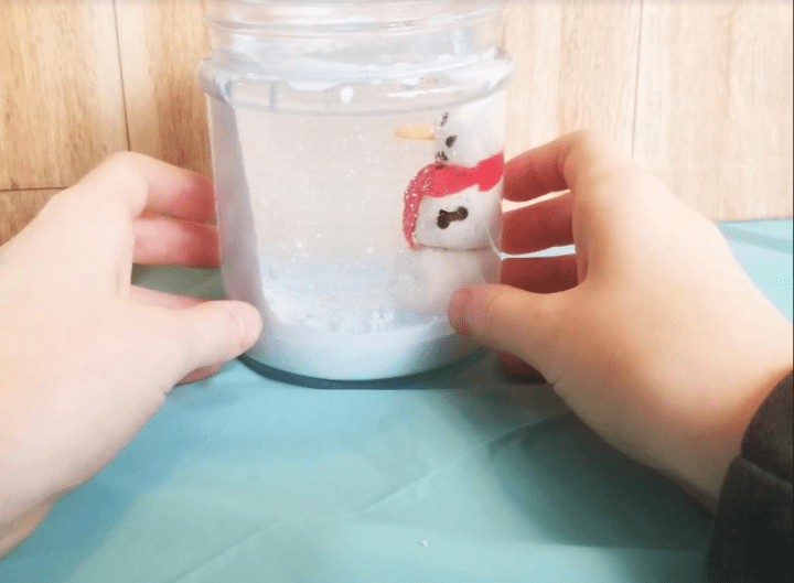 stem activity for kids showing a child holding a jar with their clay snowman and paint dripping like snow