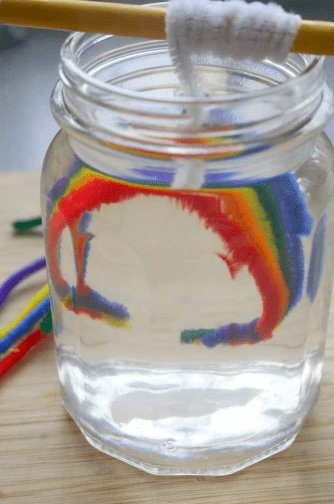 science experiments for kids shows rainbow pipe cleaners hanging in a liquid glass jar