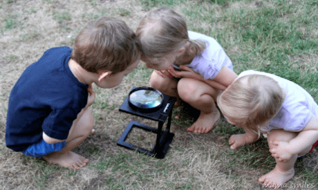 outdoor education for kids shows three children bent over looking through a microscope