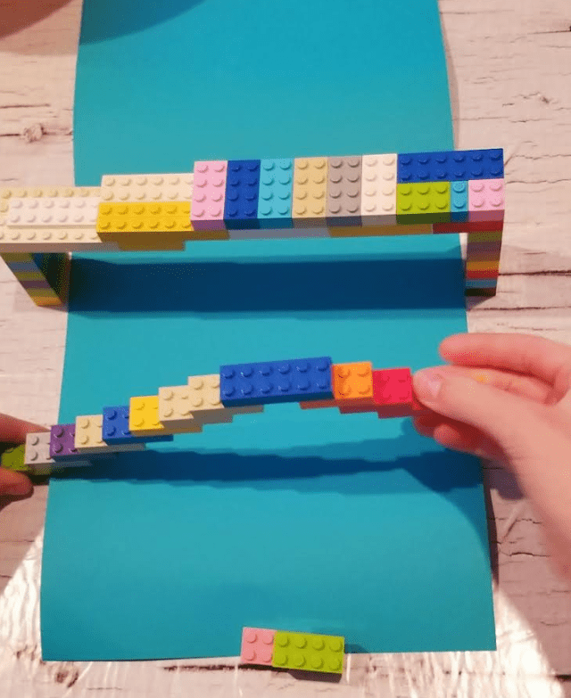 stem building challenge shows a child building a bridge with plastic building blocks