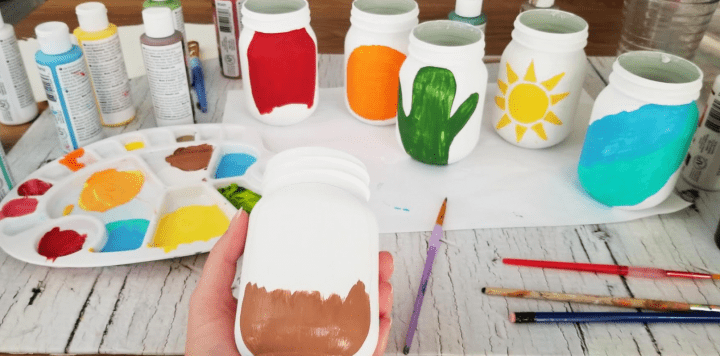 mason jar crafts for kids shows a table with unfinished jars, paints and mixing plate
