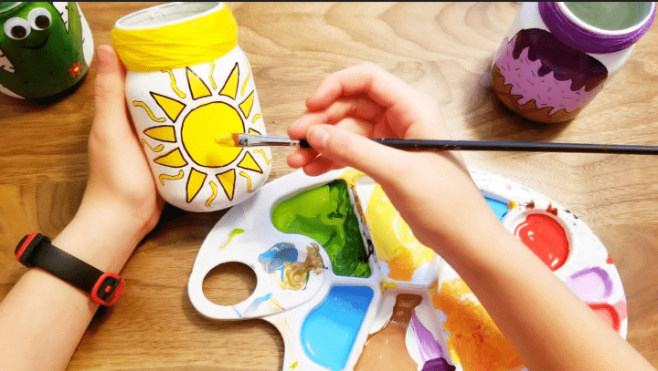 mason jar craft shows a child painting a sun on a jar