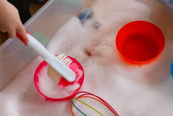 sensory play shows a child playing with a scrubber in foamy water