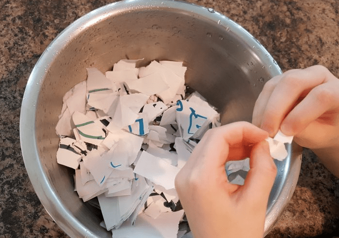 free valentines day paper mache activity shows a child ripping up pieces of paper into a bowl.