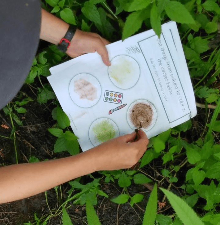 outdoor learning activity shows a child rubbing mud onto the booklet page.