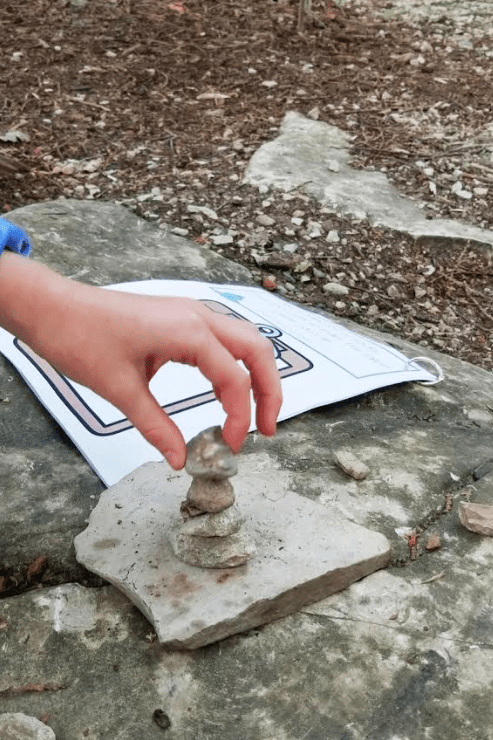 outdoor learning activities shows a child placing a rock on top of a rock tower.