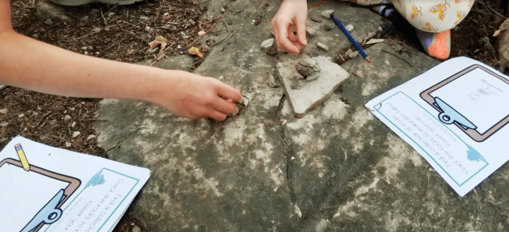 outdoor learning activities shows two children building with rocks and paper booklets in front.