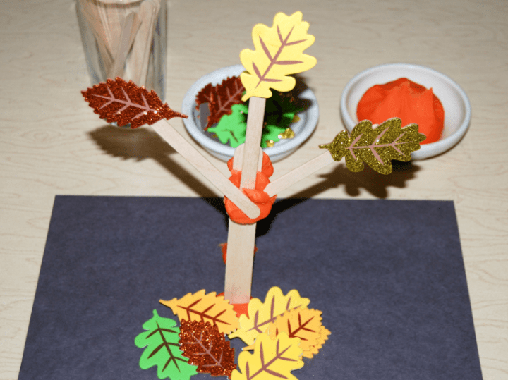 fall science experiment shows a tree structure made from popsicle sticks, playdough and fake leaves.