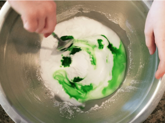 chemical reaction shows a child mixing green food coloring into the baking soda mixutre.
