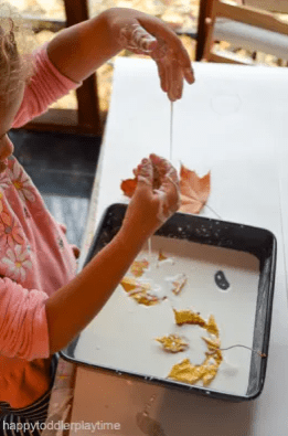 fall sensory activity shows a child playing with oobleck and leaves.