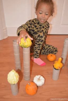 fall stem challenge shows a child balancing mini pumpkins on paper rolls.