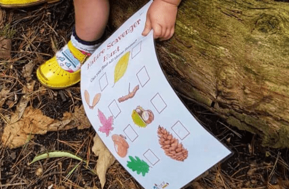 outdoor classroom shows a young child holding a printed scavenger hunt page outside.