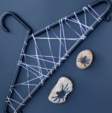 Halloween STEM shows a hanger with string wrapped around and two stones with spiders drawn on.