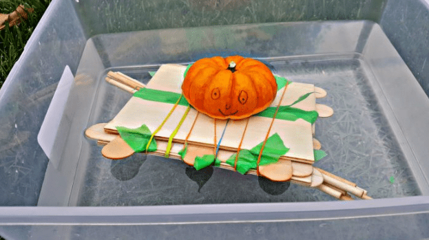 STEM challenge shows a mini pumpkin on a wooden boat made from popsicle sticks and small wood boards.