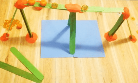 Halloween STEM activity shows a bridge made from sticks and plastic mini pumpkins on top.
