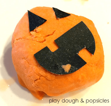 Halloween STEM activities shows a play dough pumpkin and a jack-on-lantern face cut out and stuck on top.