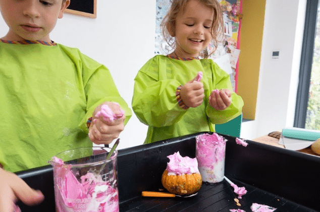 Halloween STEM activity shows two children playing with halloween foam and fizzing materials.