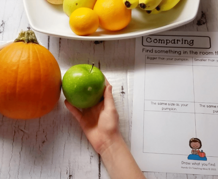 Pumpkin Investigation STEM Activities shows a child holding an apple beside a pumpkin to compare size.