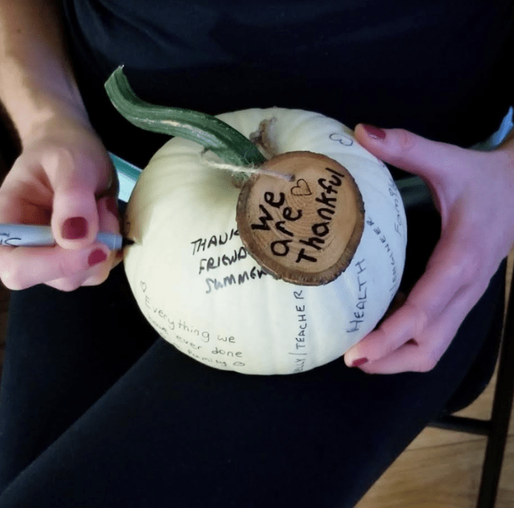 fall activity for kids shows a person writing on a white pumpkin.