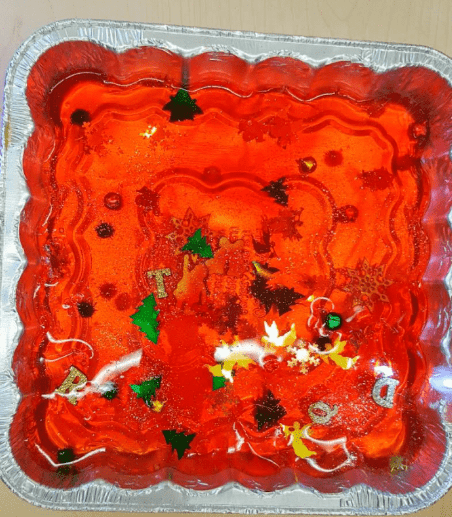 Science experiment for kids shows a tray with red Jello and gems throughout.
